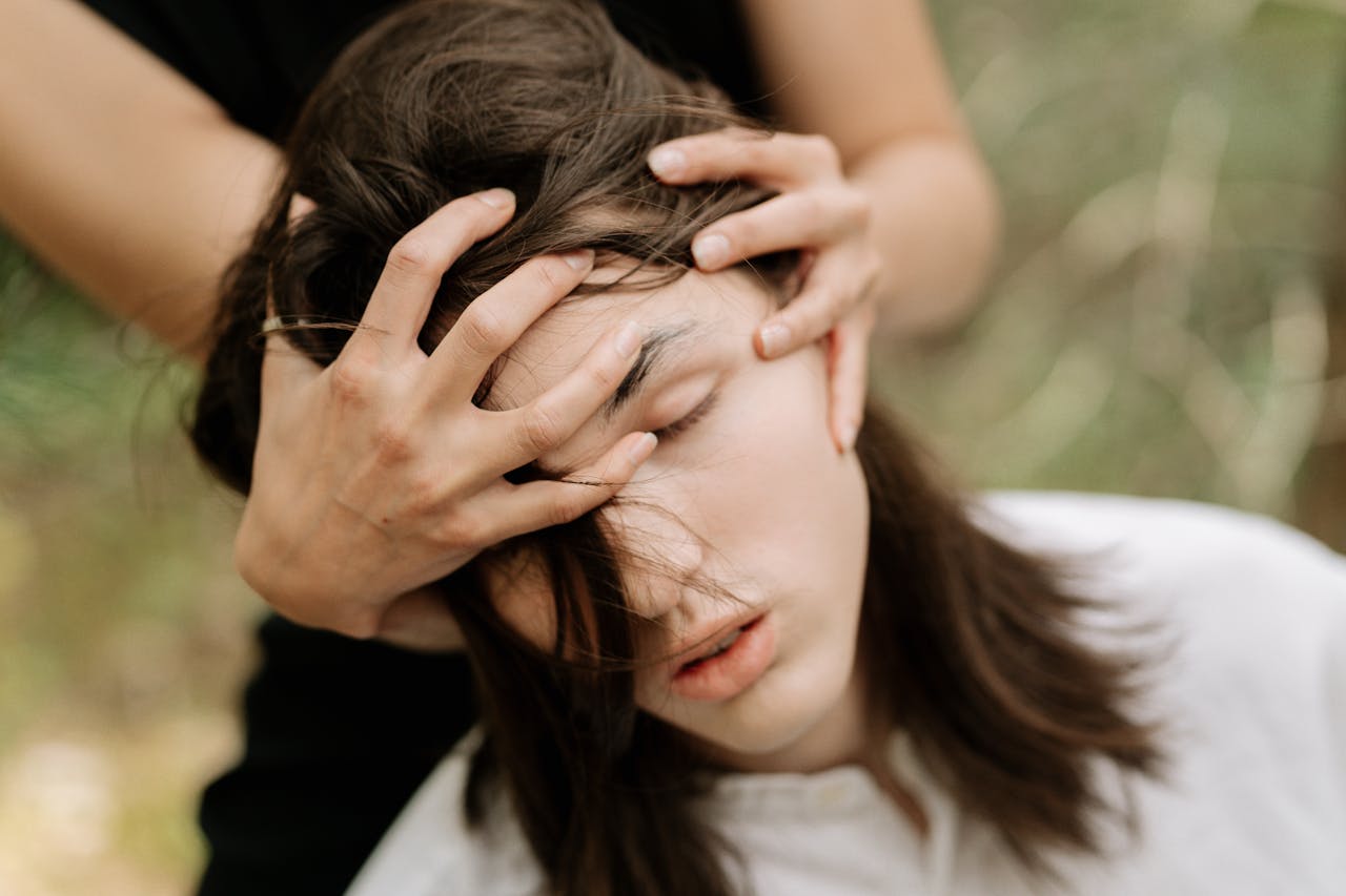 A close-up portrait of a person with hands on face, conveying emotion in an outdoor setting.
